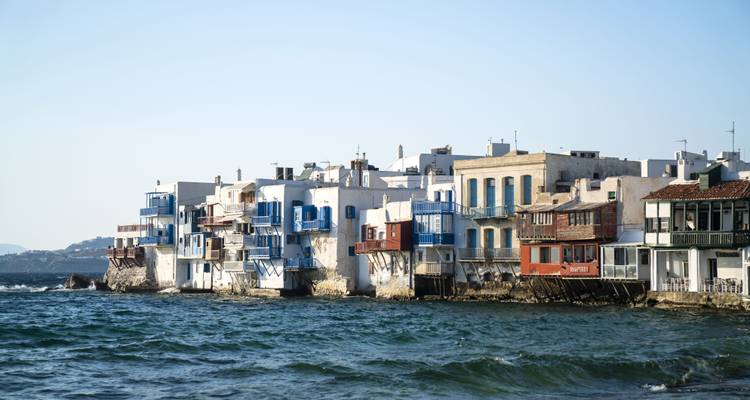 Casas encaladas con contraventanas azules bordean el frente marítimo de la Pequeña Venecia de Mykonos sobre olas agitadas