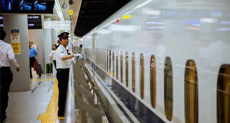 Bahnsteigszene mit einem uniformierten Schaffner, der einen schlanken weißen Shinkansen-Hochgeschwindigkeitszug vorbereitet