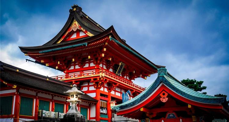 Lebendige zinnoberrote Eingangsgebäude eines Shinto-Schreins unter dramatischen Wolken in Kyoto