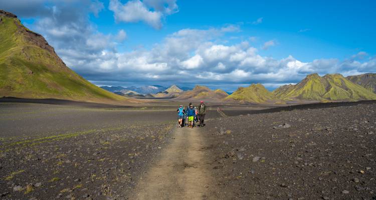 Groupe de randonneurs marchant sur un sentier avec des montagnes volcaniques en arrière-plan.