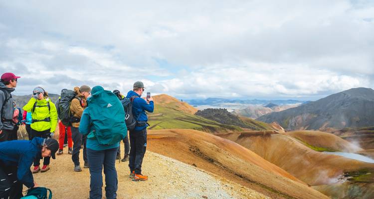 Des randonneurs s'arrêtent pour prendre des photos d'un paysage volcanique coloré.