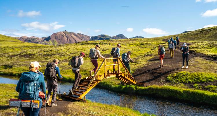 Grupo de excursionistas cruzando un pequeño puente en un paisaje vibrante.