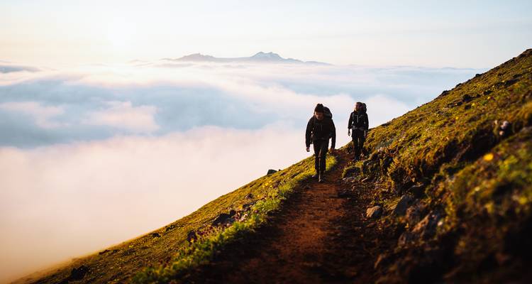 Los excursionistas ascienden por un sendero de alta montaña sobre un mar de nubes al amanecer.