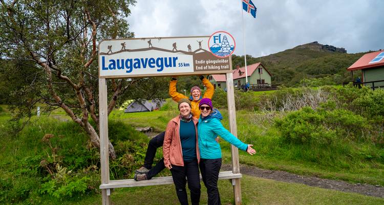 Les voyageurs célèbrent au panneau de fin du sentier de Laugavegur avec le drapeau islandais à proximité