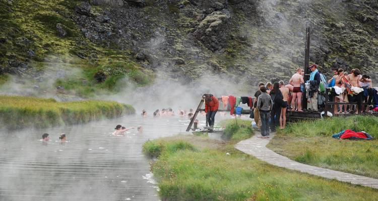 Des gens se baignant dans une source chaude naturelle au milieu d'un terrain rocheux verdoyant.