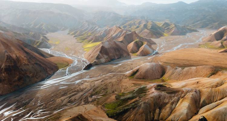 Vue aérienne d'un paysage volcanique vallonné et coloré avec des rivières.