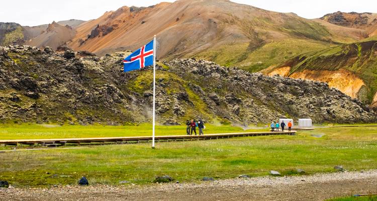 Paysage avec collines rocheuses, drapeau islandais et vapeur s'élevant au loin.