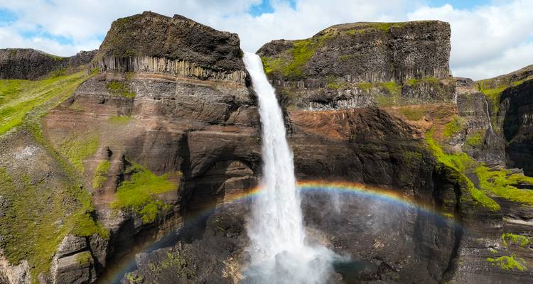 Gran cascada con efecto de arcoíris frente a acantilados rocosos.