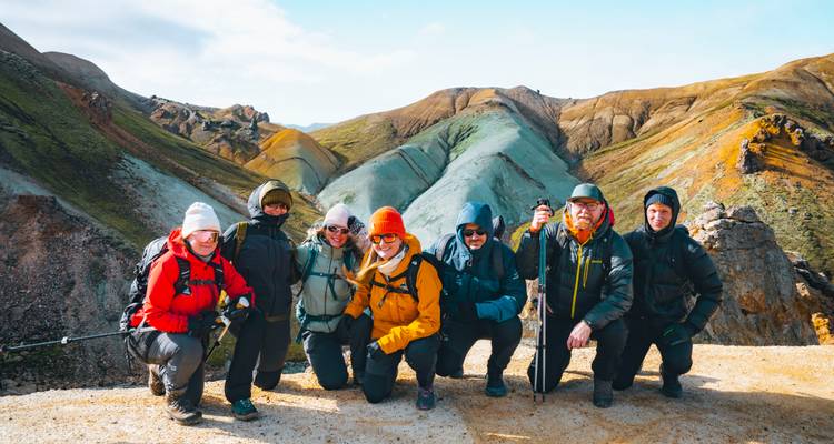 Grupo sonriente de excursionistas abrigados posan juntos en una cresta volcánica colorida durante su caminata.