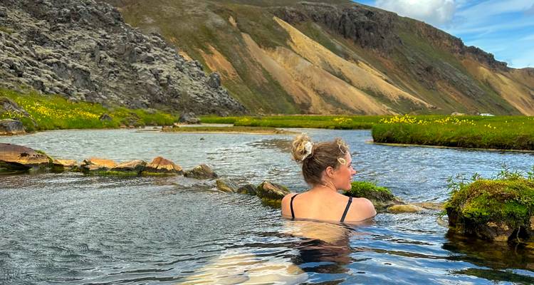 Young woman relaxing in a natural geothermal stream surrounded by mountains.