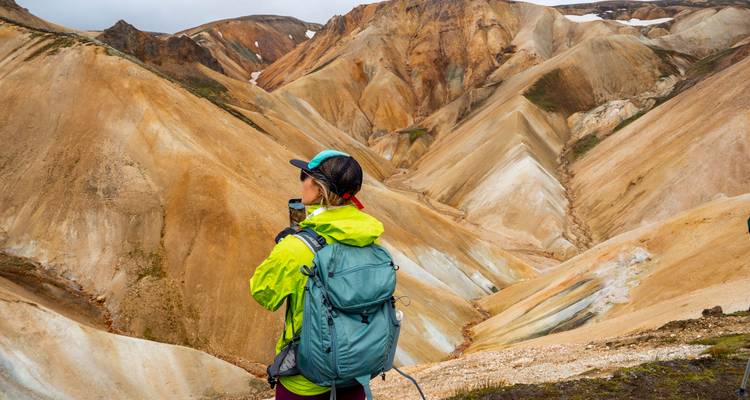 Back-view of a lone hiker with backpack admiring streaked rhyolite hills.