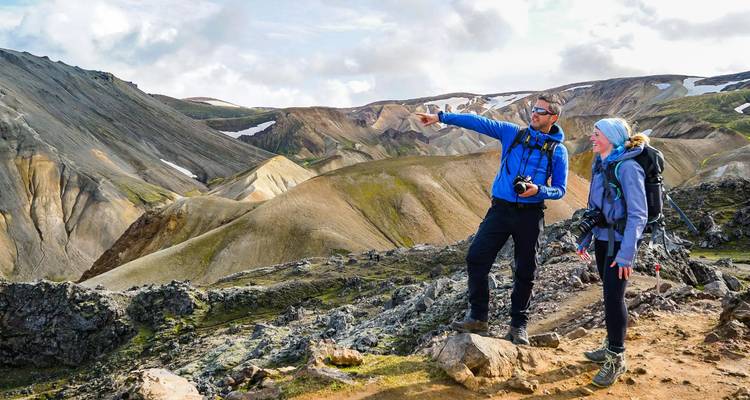 Two hikers consult the view, pointing across multihued volcanic ridges in Iceland.