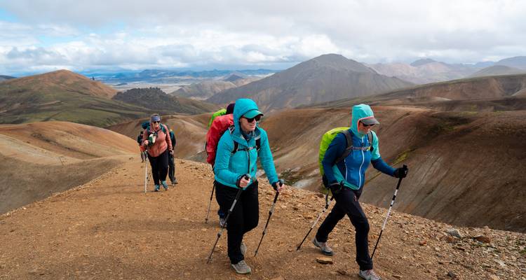 Bundle-clad hikers trek a windy ridge surrounded by vast volcanic landscapes.