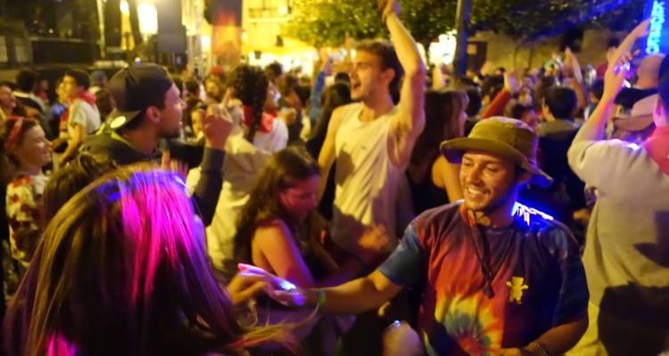 Crowd of people dancing at a night event, colorful lights illuminate the scene.