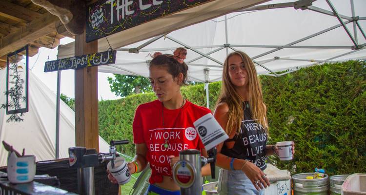 Two women serving drinks in festival booth.
