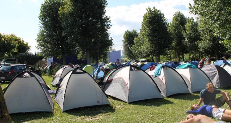 Camping avec des rangées de tentes, des arbres et un ciel bleu.