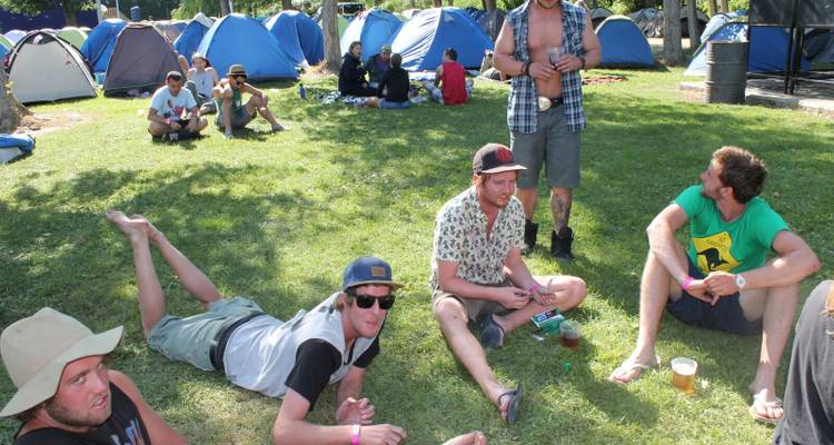 Groupe d'amis se détendant sur l'herbe avec des tentes visibles.