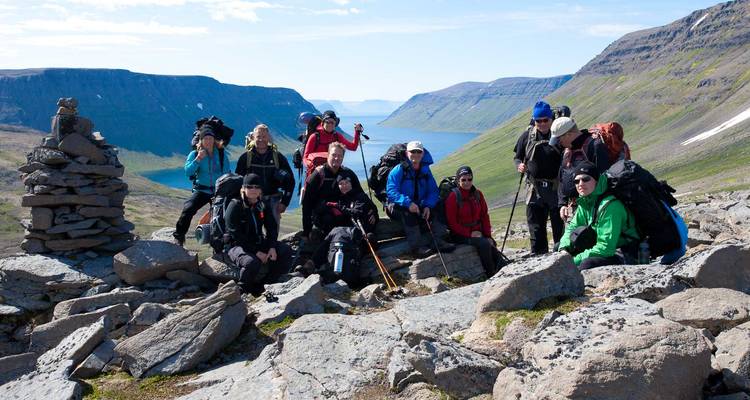 Eine Wandergruppe posiert auf felsigem Gelande mit Blick auf tiefe Fjorde und das entfernte Meer.