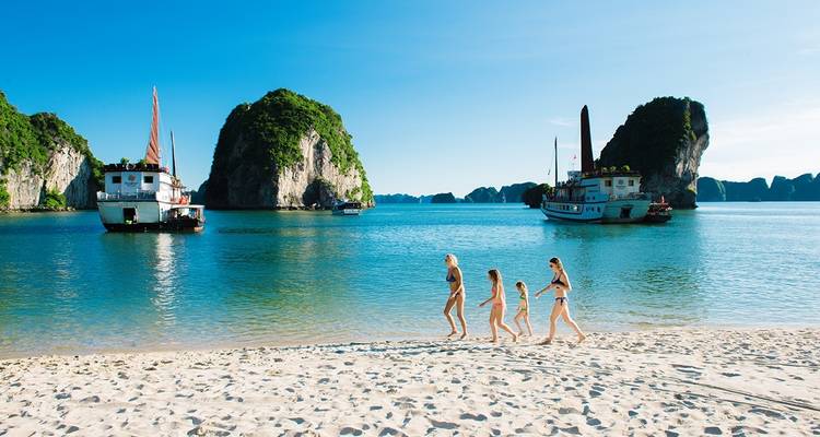 Family walking on a beach with scenic karst formations.