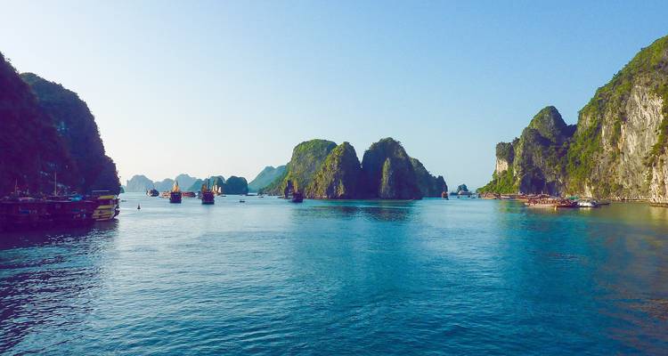 Panoramic view of limestone karsts and boats on clear blue waters.
