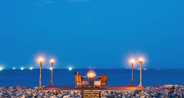Romantisches Abendessen auf einer Holzplattform am Meer bei Nacht.