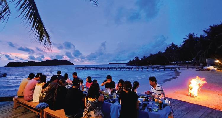 Un grand groupe profitant d'un dîner en bord de plage à côté d'un feu de camp au crépuscule sur l'île de Phu Quoc.