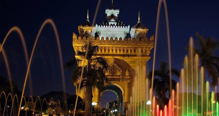 Arco del monumento iluminado por la noche con fuentes de agua de colores.