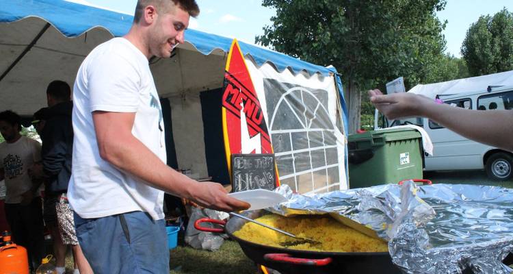 Man serving food from a large pan at an outdoor gathering.