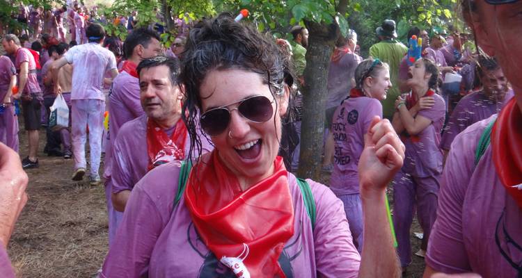Smiling woman in sunglasses at an outdoor festival, surrounded by people.