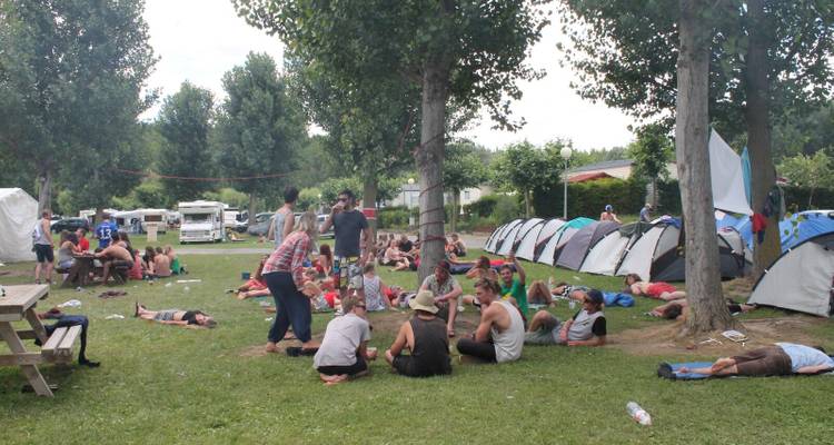 People relaxing on a campsite with tents and trees around.