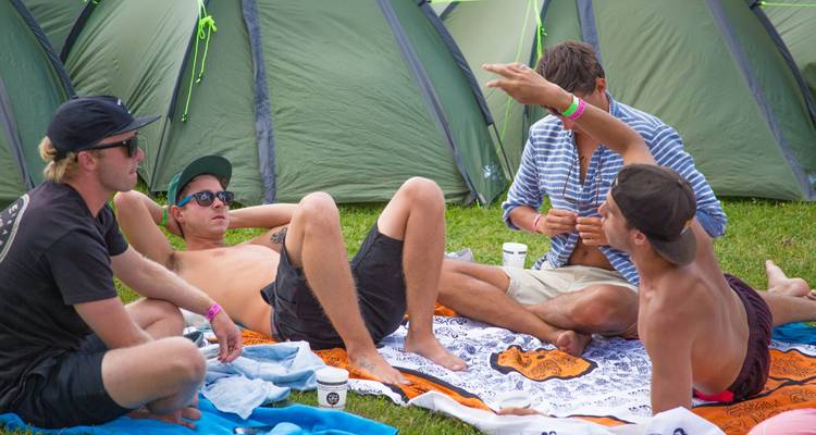 Group of friends relaxing on blankets outside tents.
