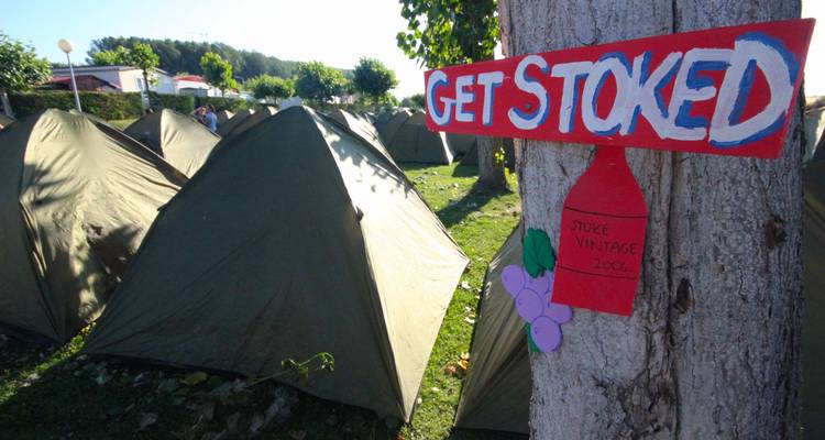 Tents set up with a 'Get Stoked' sign on tree.
