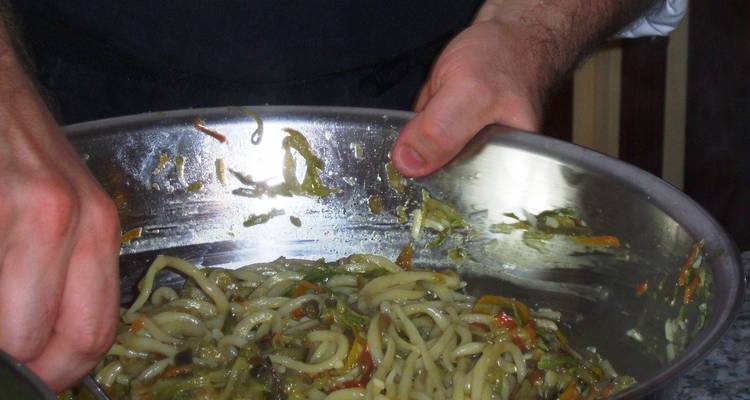 Primer plano de una persona revolviendo un tazón grande de pasta con verduras.