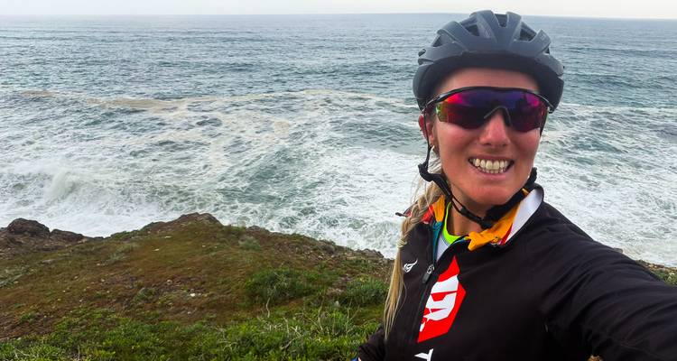 Una ciclista se toma una selfie en el borde de un acantilado con las olas del Atlántico estrellándose de fondo.