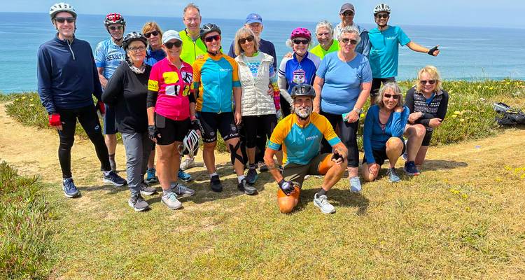 Un gran grupo de ciclistas posa en la cima de un acantilado cubierto de hierba que domina el Atlántico azul.