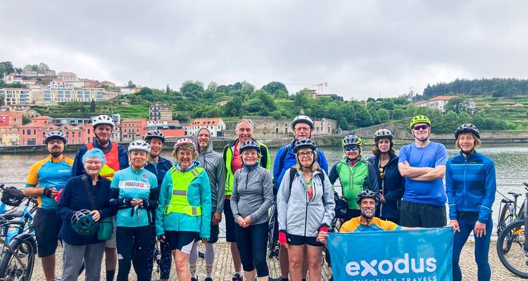 Ciclistas con un estandarte de Exodus se reúnen junto a un paisaje urbano de río bajo cielos grises.