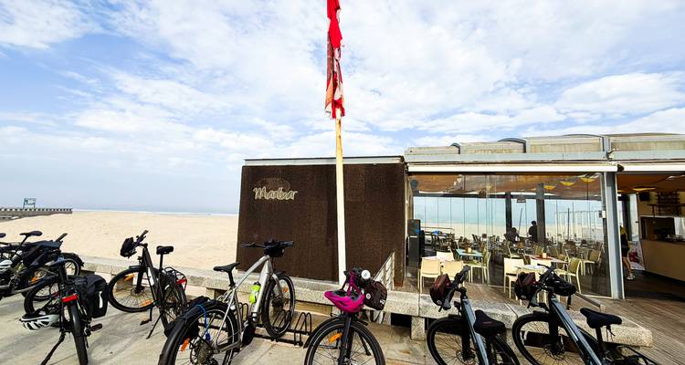 Las bicicletas de alquiler están afuera de un café frente a la playa con arenas amplias y un cielo nublado.