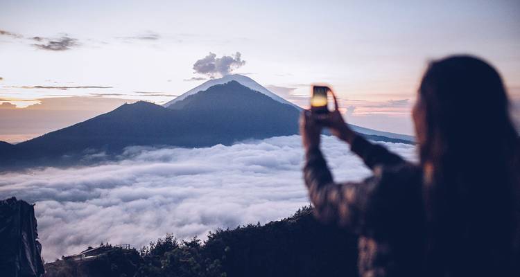 Reiziger die de Mount Batur fotografeert die boven een zee van wolken tijdens zonsopgang uitkomt