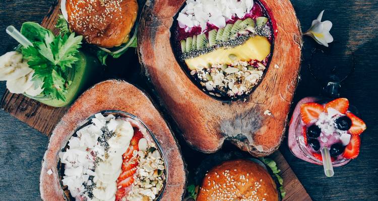 Kleurrijke smoothie bowls, burgers en verse sappen gerangschikt op een houten tafel in een Balinese cafe