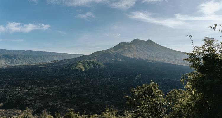 Uitgestrekt lavaveld met de Batur-berg die oprijst onder een heldere blauwe lucht