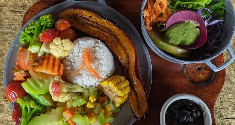 Bunte costaricanische Mahlzeit mit Reis, Gemüse, Kochbanane und Beilagensaucen auf Holztisch.