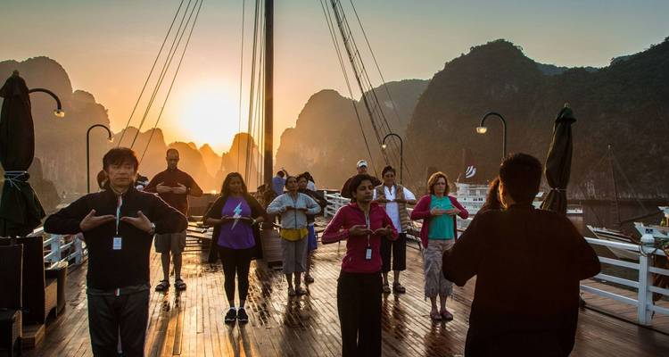 Group of people practicing tai chi on a deck at sunrise near Halong Bay