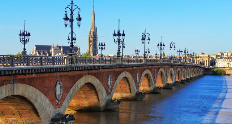 Pont de pierre traversant une rivière avec un paysage urbain et une église en arrière-plan.