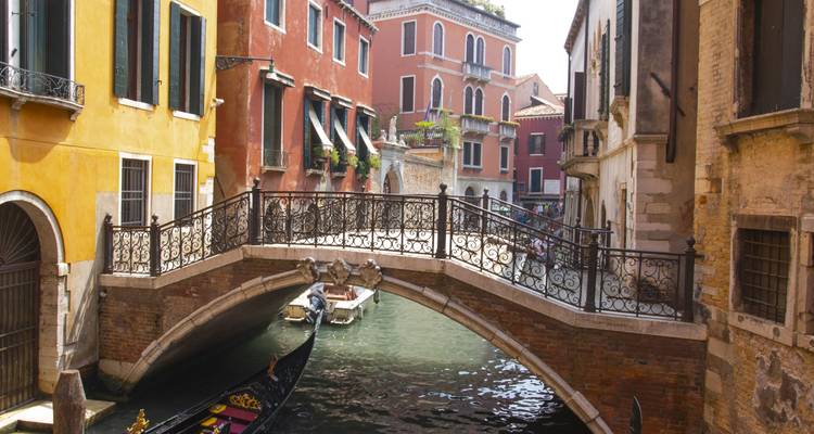 Canal vénitien avec un pont décoratif et une gondole qui passe dessous.