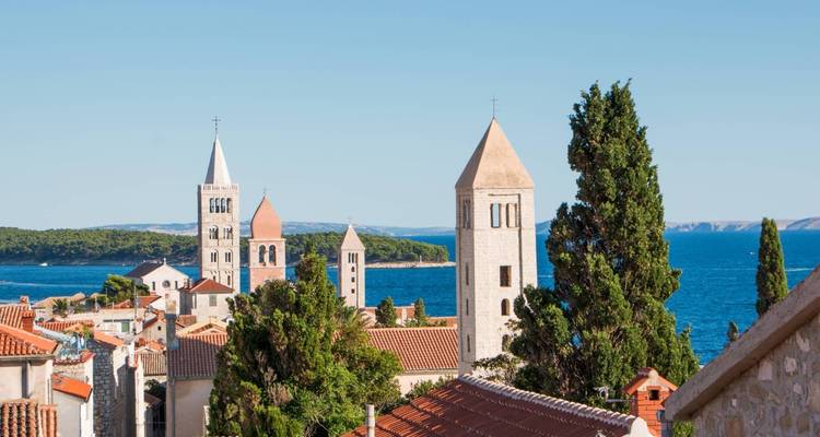 Vista de un paisaje urbano histórico con torres de iglesia y el mar de fondo.