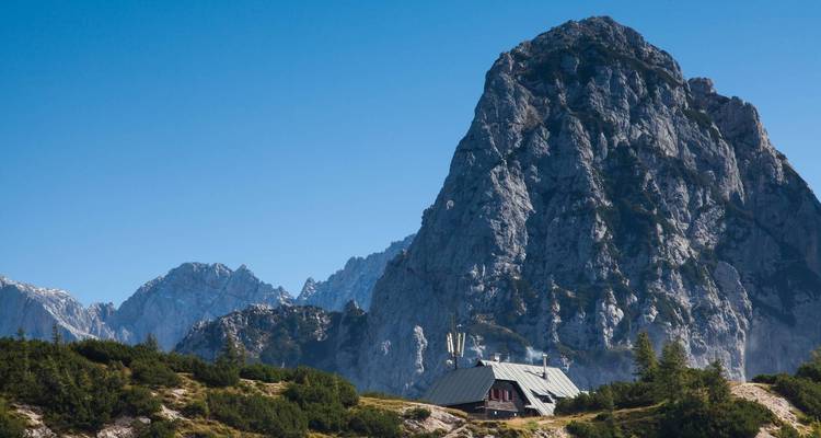 Montaña rocosa alta con una cabaña en su base.