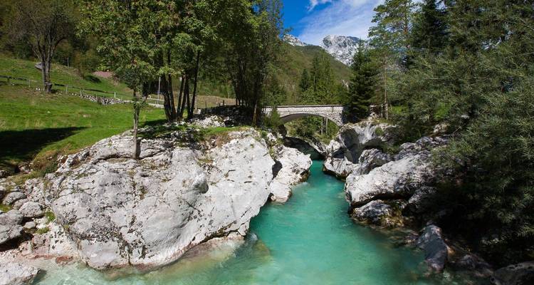 Río turquesa cristalino que pasa bajo un viejo puente de piedra.