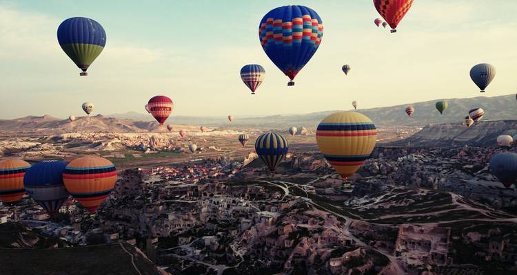Decenas de globos aerostáticos de colores brillantes flotan sobre el paisaje accidentado de Capadocia al amanecer.