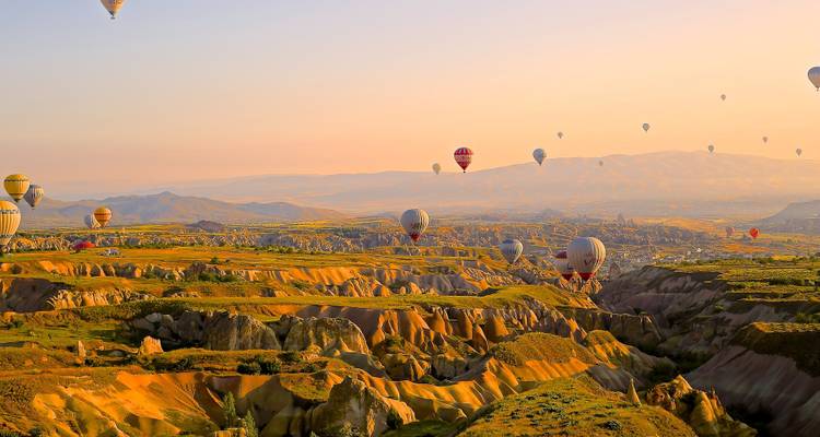 Los globos aerostáticos flotan sobre los dorados valles rocosos de Capadocia bañados por la cálida luz del amanecer.