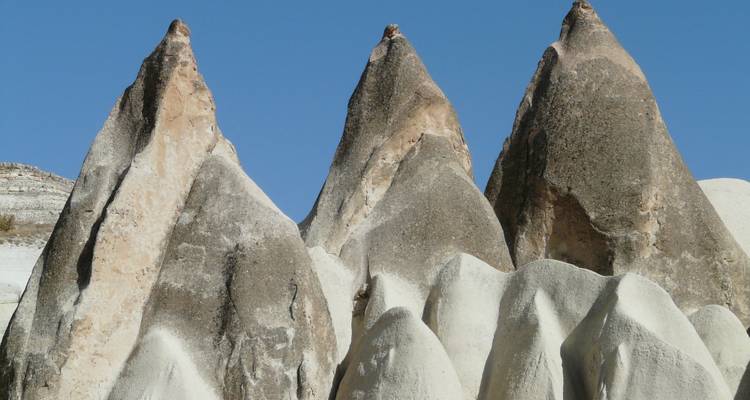 Primer plano de tres puntiagudas chimeneas de hadas de roca contra un cielo azul despejado en Capadocia.